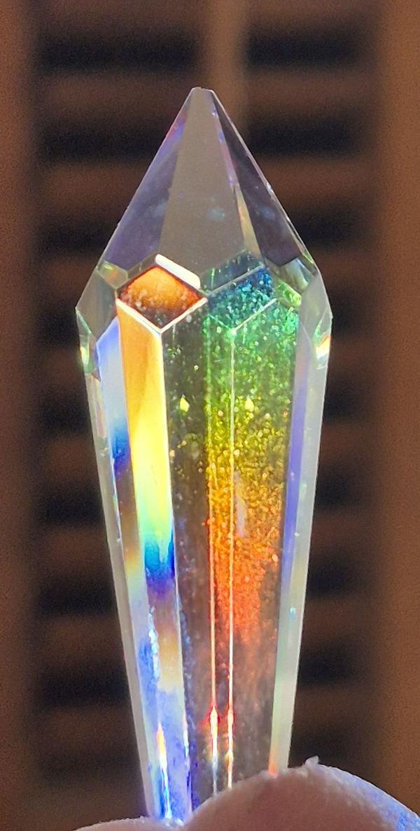 A SunRain prism suncatcher hanging in direct sunlight, casting high-contrast, vivid rainbow bands across a room