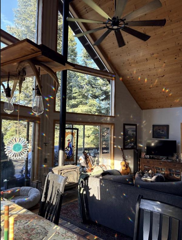 Three custom SunRain suncatchers hanging from a rustic antler chandelier in a California cabin with floor-to-ceiling glass
