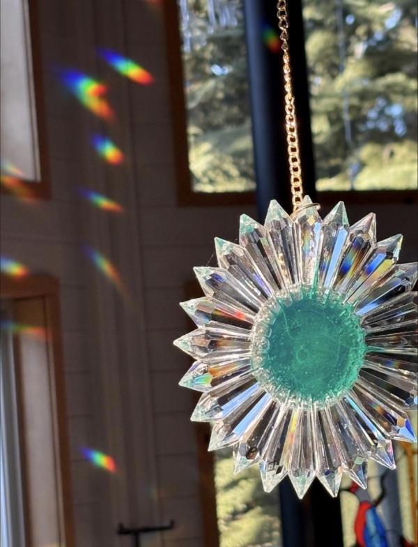 Close-up of a green SunRain suncatcher casting rich rainbows across the darkened interior wood walls of a cabin